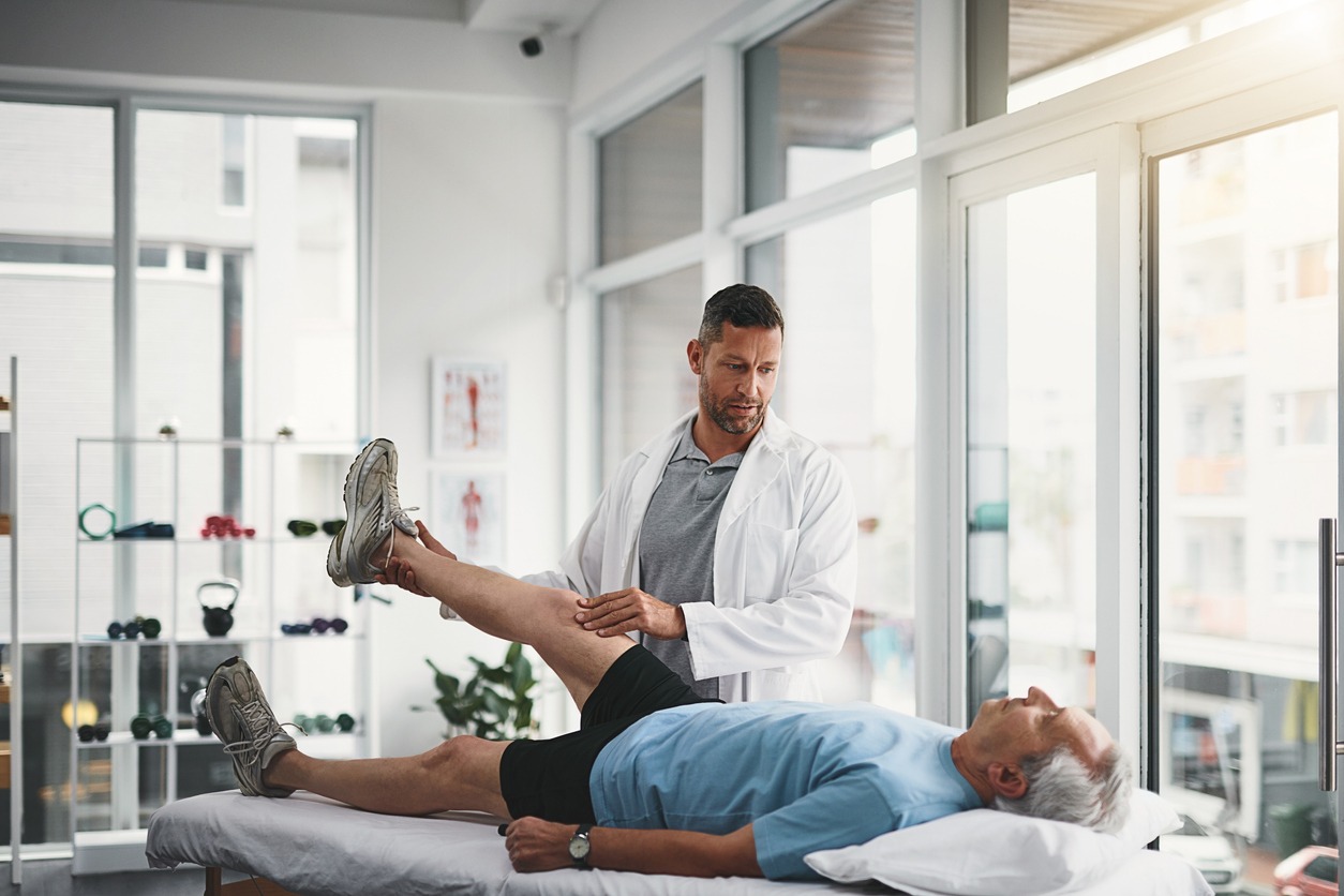 physical therapist assessing elderly patient’s leg movement in clinic